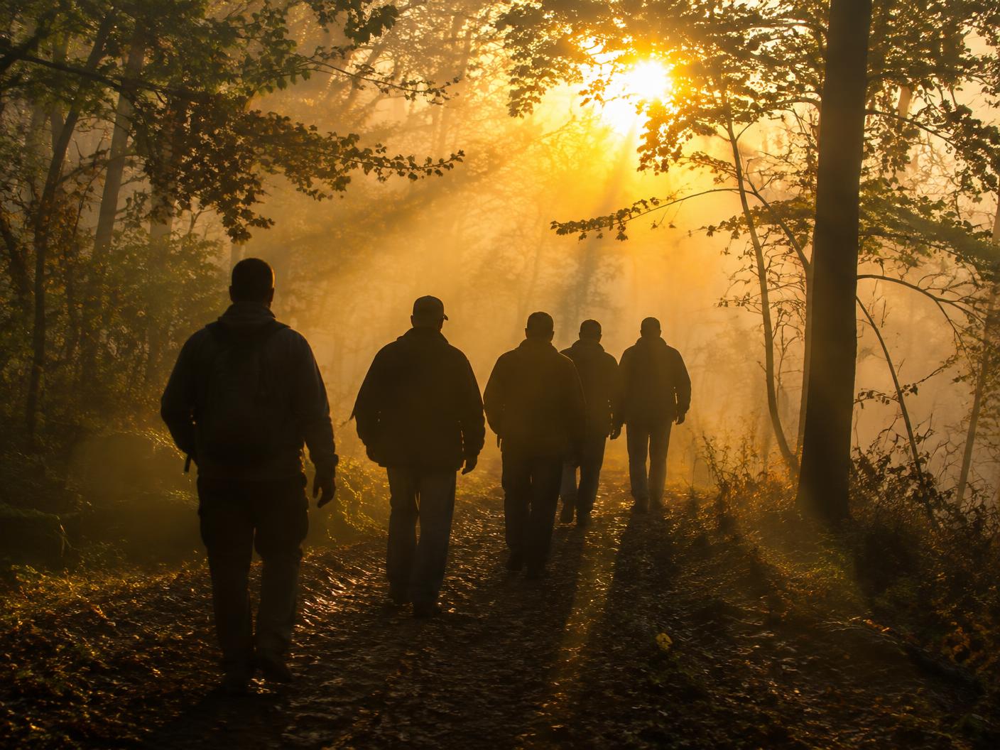 Men walking a wooded trail at sunrise during a prayer retreat